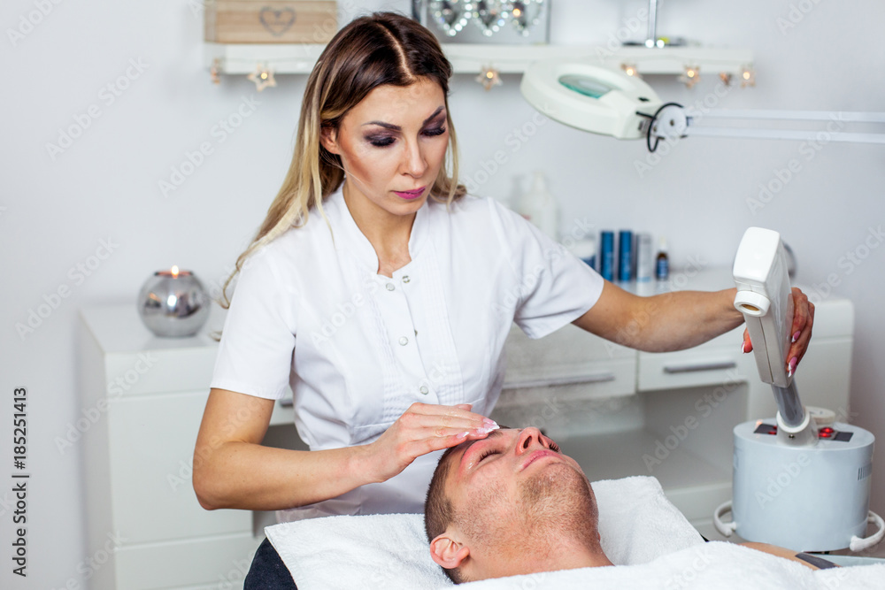 Cosmetologist is doing procedure of face massage for young boy / man. Model, close-up. Cosmetological clinic. Healthcare Cosmetologist is doing procedure of face massage for young boy / man. Model, close-up. Cosmetological clinic. Healthcare
