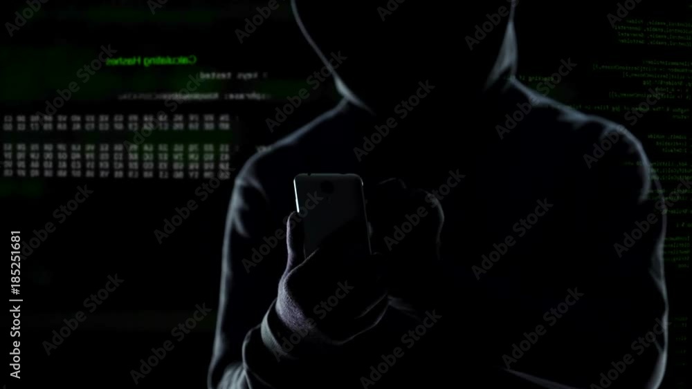 Close up of hooded hacker initiating cyber attack on smartphone, launching bomb Close up of hooded hacker initiating cyber attack on smartphone, launching bomb