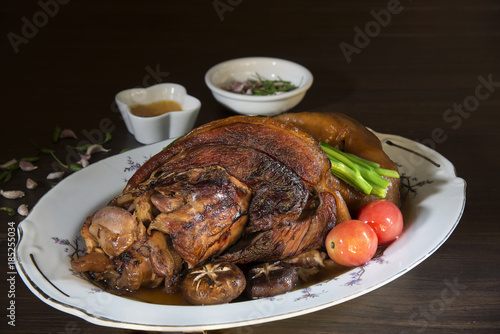 Stewed pork leg in gravy sauce and vegetable on white dish on wooden background with dim light. Chinese food. Still Life image and Selective focus.