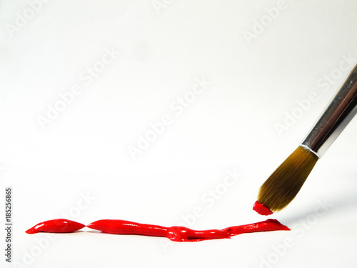 Brush with red paint over a strip of acrylic paint squeezed out of the tube.