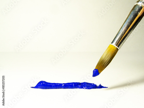 Brush with blue paint next to a strip of acrylic paint squeezed out of the tube.