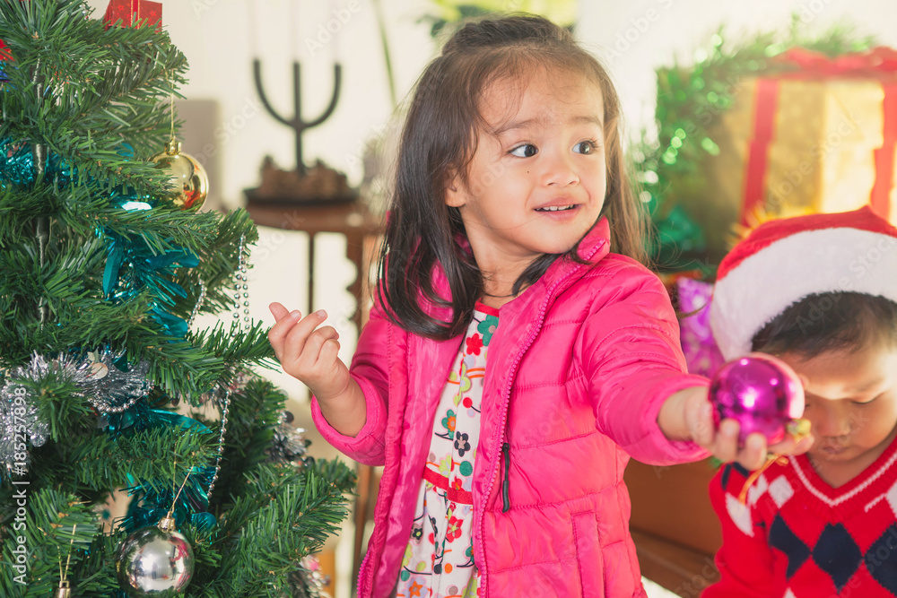 Happy little smiling girl with christmas party. Little siblings decorating christmas tree together at home. Happy little smiling girl with christmas party. Little siblings decorating christmas tree together at home.