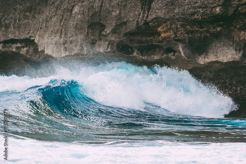 Blue crystal wave and rocks in ocean.