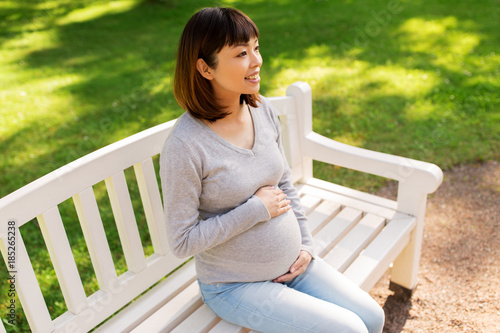 happy pregnant asian woman sitting on park bench