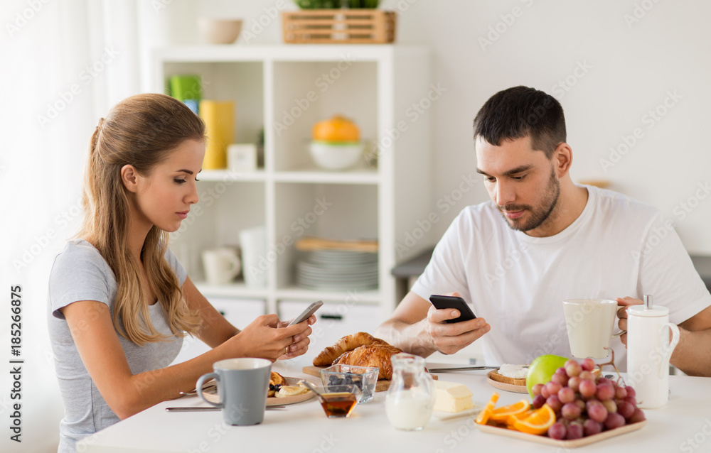 couple with smartphones having breakfast at home