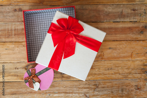 White gift box and red ribbon and mini heart inside on wood background with space..