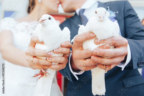 Two white pigeons in the hands of a wedding couple. Kiss in the background