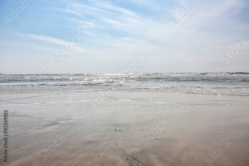 Sitting on the ocean beach, view at the waves in the sun with clouds in the sky
