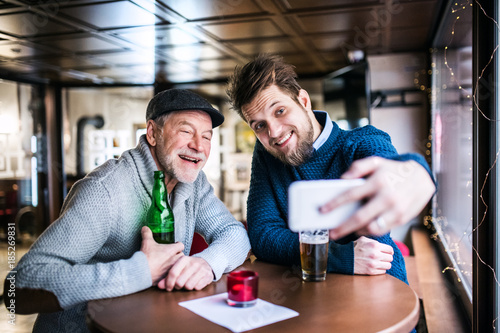 Senior father and his young son with smartphone in a pub.