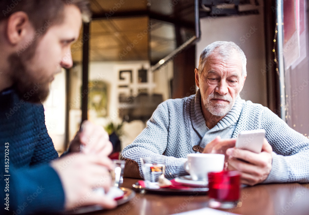 Senior father with smartphone and young son in a cafe. Senior father with smartphone and young son in a cafe.