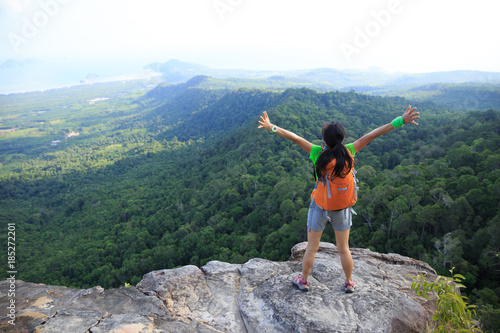 successful woman hiker open arms at cliff edge on mountain top
