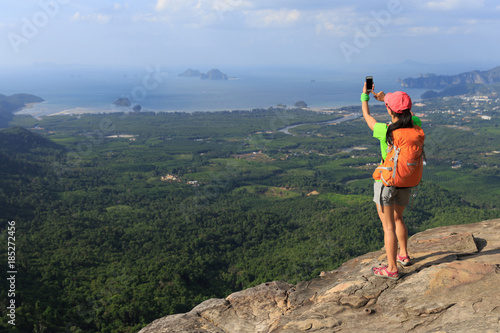 successful woman hiker taking picture with smartphone at cliff edge on mountain top