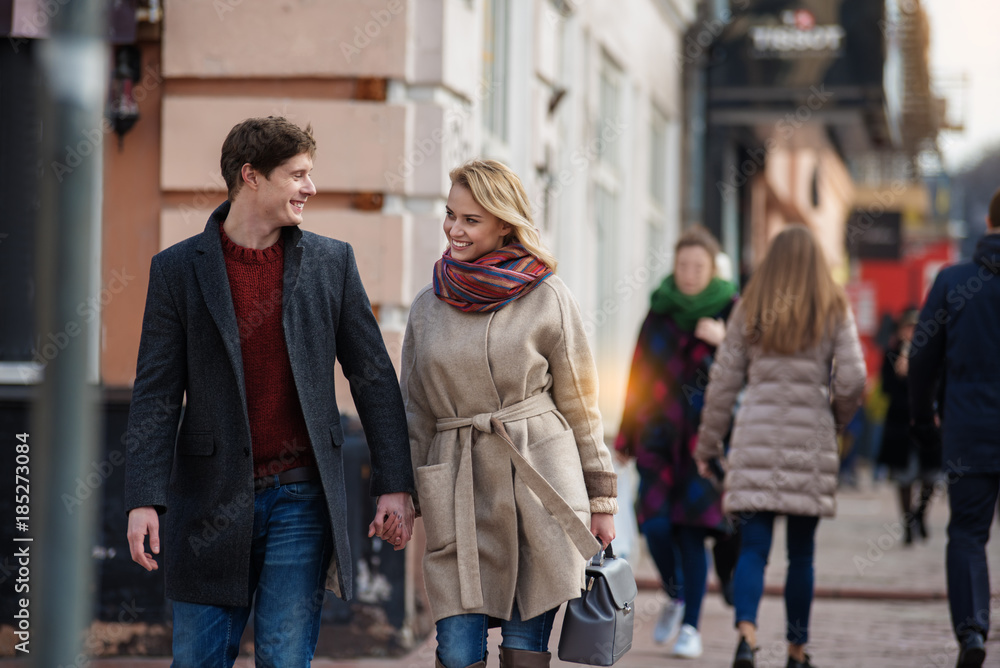 Obraz premium Portrait of young man and woman walking down the street and looking at each other with people on the background