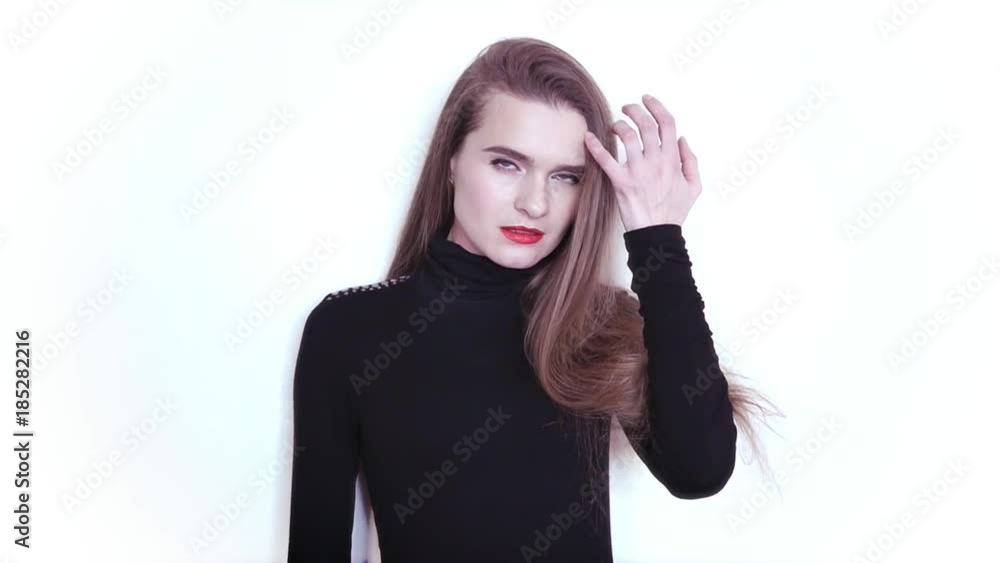 Attractive young girl stands on white background posing at camera holding hand over hair. HD, 1920x1080, slow motion Attractive young girl stands on white background posing at camera holding hand over hair. HD, 1920x1080, slow motion