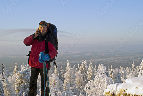 Billede på lærred smiling traveler man at the top of a mountain talking on a mobile phone in the b