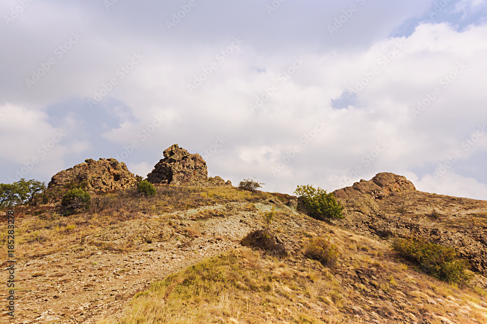 The top of the mountain with rocks,bushes and dry grass on the sky background.
