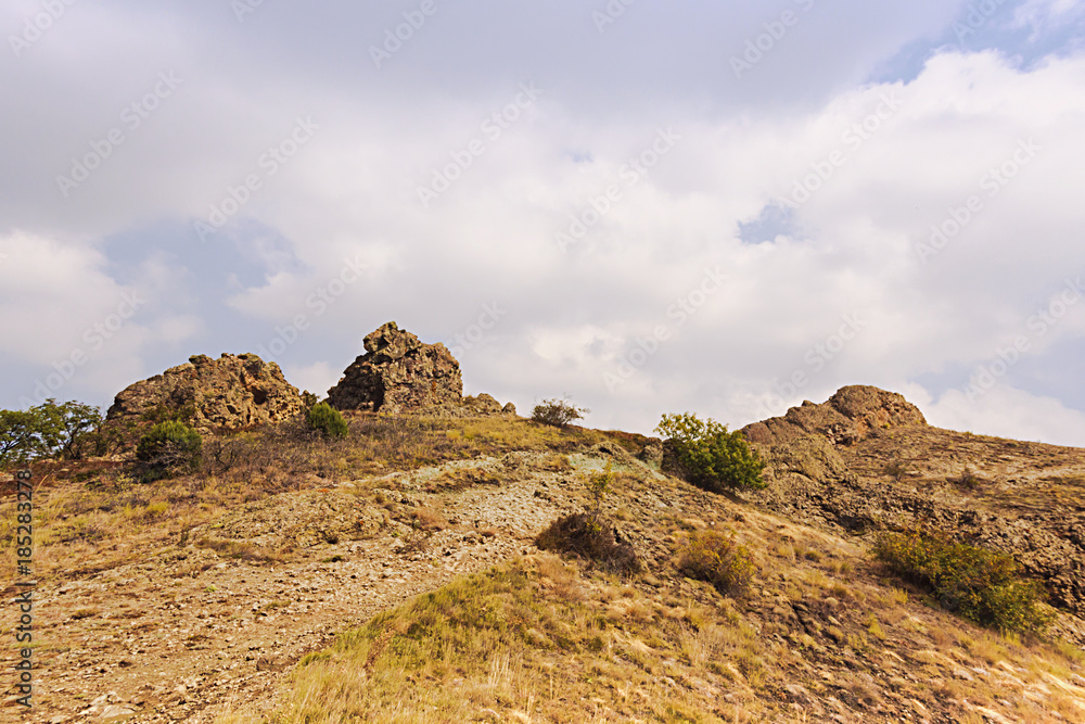 The top of the mountain with rocks,bushes and dry grass on the sky background. The top of the mountain with rocks,bushes and dry grass on the sky background.