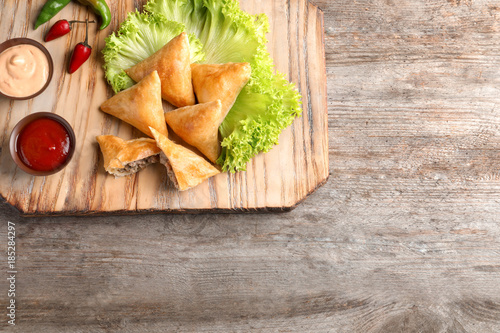 Wooden board with delicious meat samosas on table
