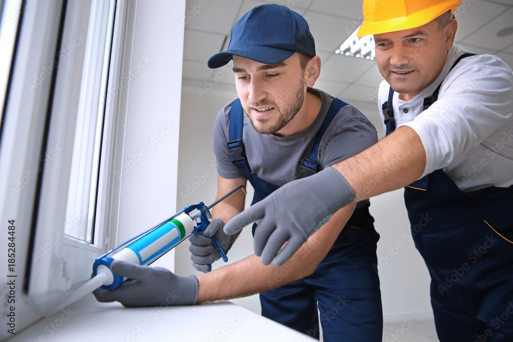 Construction worker with trainee installing window in house Construction worker with trainee installing window in house