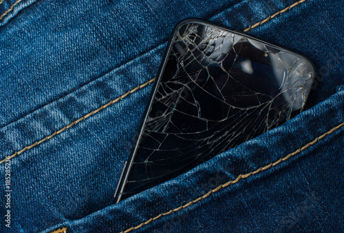 Mobile phone with a broken screen in the pocket of blue jeans.