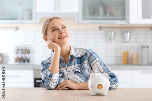 Young woman with piggy bank at table indoors