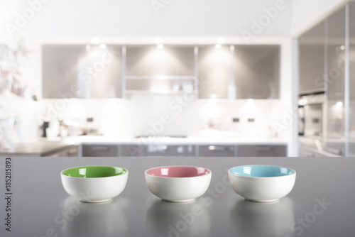 Three colored bowls on steel kitchen top with blur kitchen in the background
