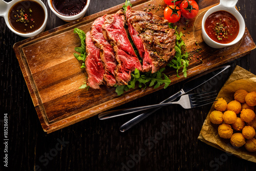 Juicy rare sliced grilled fillet steak served with tomatoes and roast vegetables on an old wooden board.