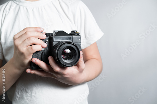 old SLR film camera in the hands of a child in a white t-shirt