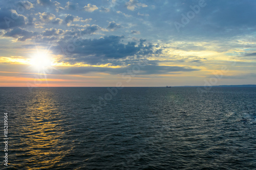 Picturesque sea landscape - the sun rises over the sea against a cloudy sky and in the distance you can see the ship and land. © WDnet Studio
