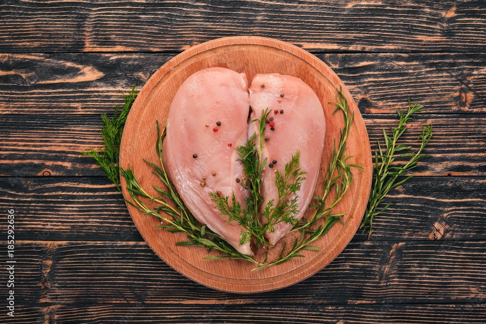 Raw chicken breast fillet with rosemary and spices on a black wooden background. Top view. Free space for text.