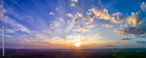 Panoramic sunset with light, puffy clouds in the sky overlooking summer New England forests. High resolution HDR panorama from drone