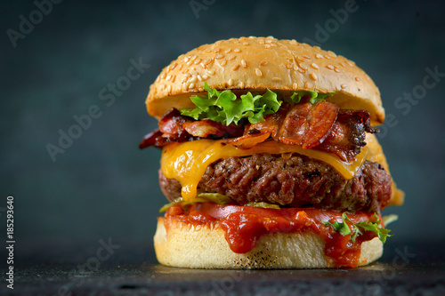 Tablou canvas Burger with cheese and bacon on a dark background