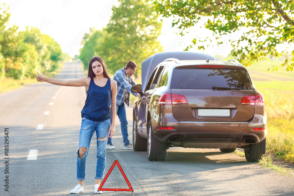 Young woman and man with broken car on background Young woman and man with broken car on background