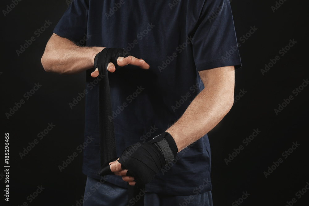 Male boxer applying wrist wraps on black background, closeup