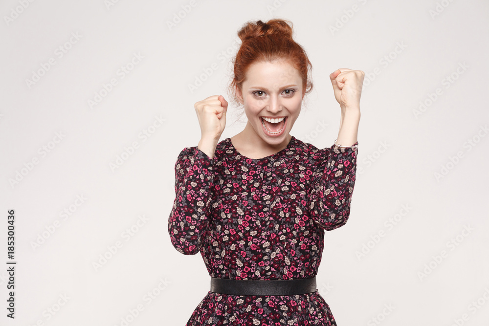 Win and success concept. Redhead woman rejoicing for his success. Isolated on gray background. Win and success concept. Redhead woman rejoicing for his success. Isolated on gray background.