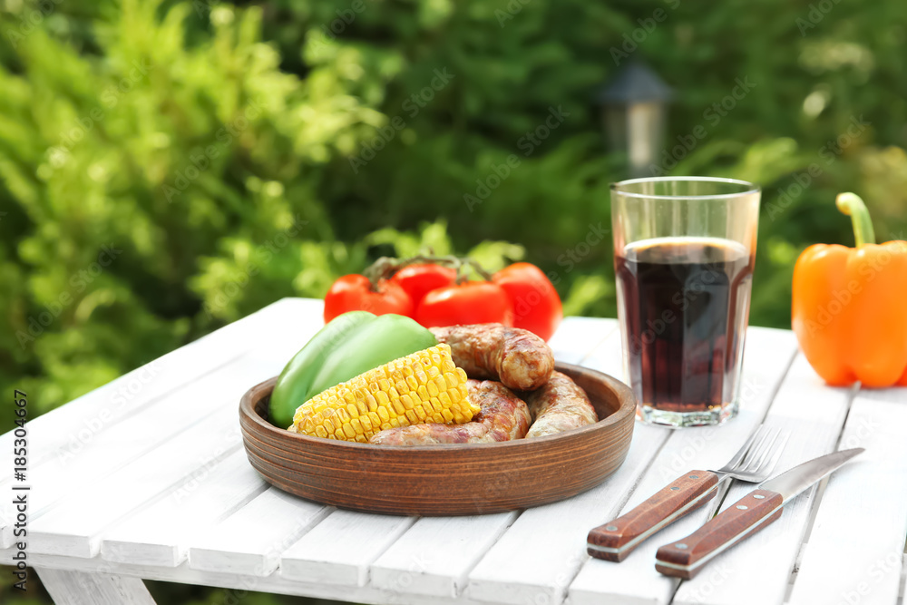 Plate with delicious grilled sausages and vegetables on wooden table outdoors
