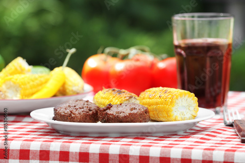 Plate with delicious grilled patties and corn cobs on table