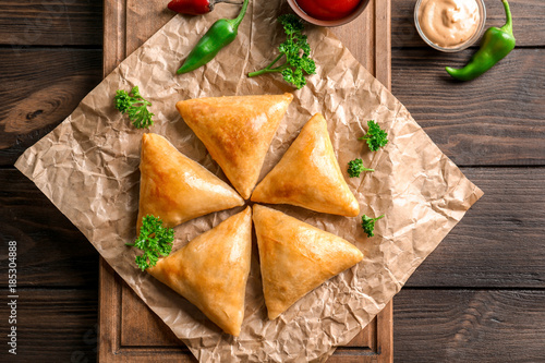 Wooden board with delicious samosas on table