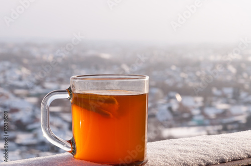 Transparent cup with hot spicy drink, lemon and orange on the background of the winter city