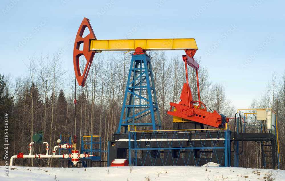 a bright pumpjack over an oil well in a winter snowy forest landscape