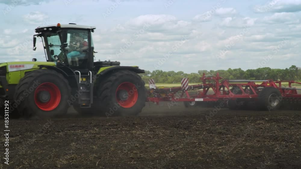 Agricultural tractor with trailer for plowing working on farming field. Farming tractor plowing arable field. Agricultural equipment Agricultural tractor with trailer for plowing working on farming field. Farming tractor plowing arable field. Agricultural equipment
