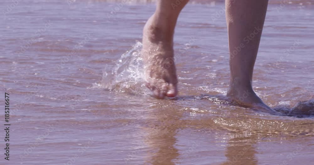 Woman feet walking through ocean waves on beach - slow motion close up Woman feet walking through ocean waves on beach - slow motion close up