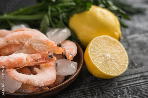 Frozen shrimp with lemon and herbs on clay bowl on black wooden table.
