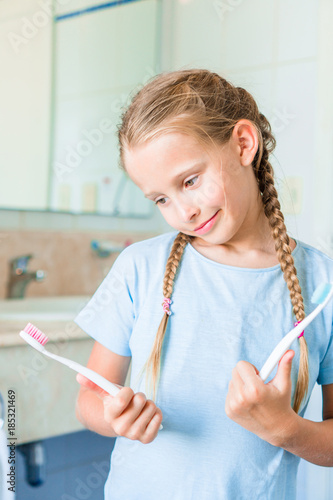 Little beautiful girl with white teeth with toothbrushes in hands in the bathroom