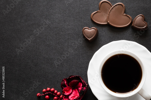 Cup of black coffee with chocolate hearts on the dark table. Enjoying a coffee and candies with beloved on the date. Empty place for a text.