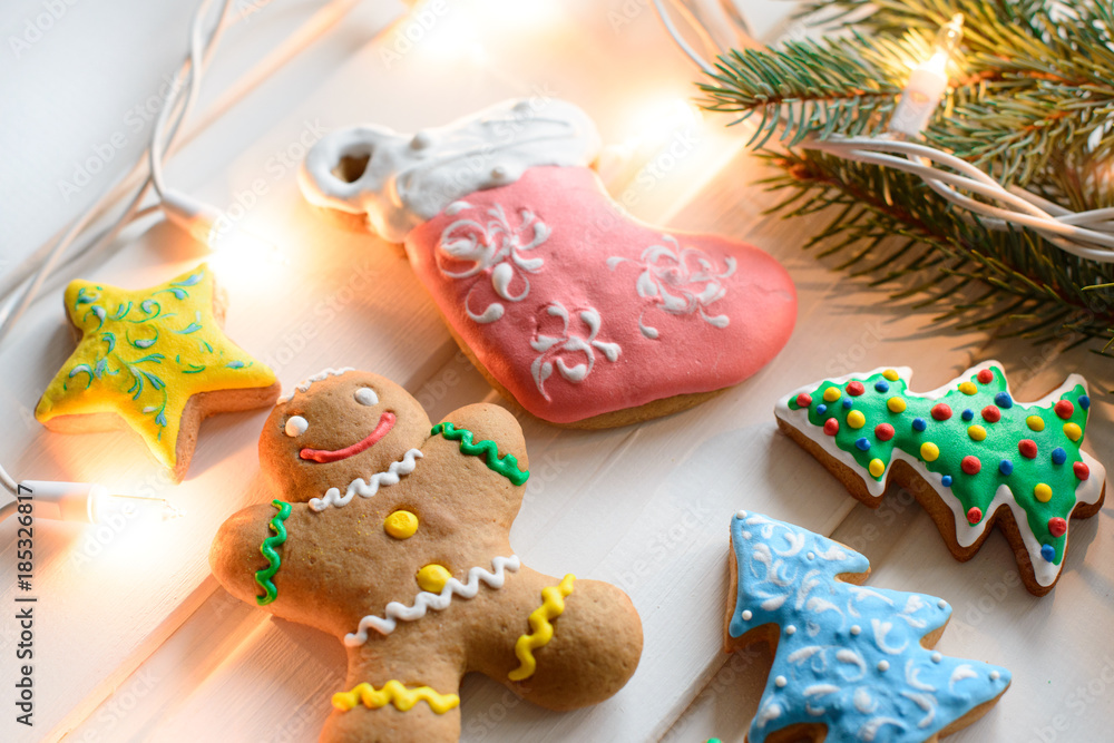 Christmas cookies with festive decoration and christmas lights on white wooden background.