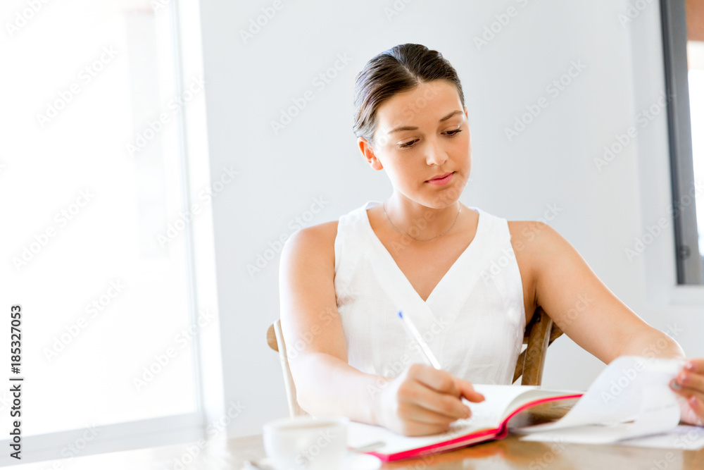 Obraz premium Young woman writing in an agenda at home or office
