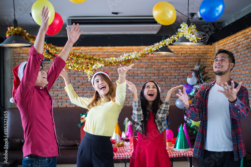 Asian man and woman wear santa claus hat having fun in Christmas party,dancing and playing balloons at the restaurant, Concept of Christmas party or New Year's party.