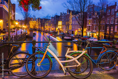 Night illumination of Amsterdam canal and bridge with typical dutch houses  boats and bicycles.