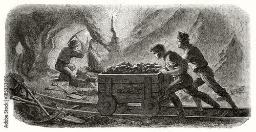 Ancient miners pulling a cart on a rail in a quartz mine at the soft light of a candle while another one is working with a pickaxe. By Chassevent and Sargent published on Le Tour du Monde Paris 1862 photo